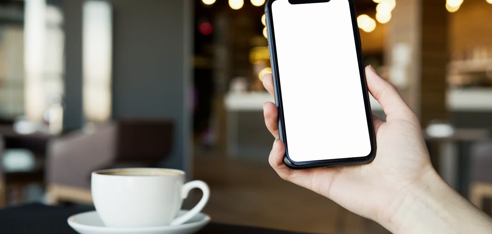 Main tenant un smartphone à côté d'une tasse de café